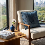 Load image into Gallery viewer, A cream bouclé armchair with a blue patterned throw pillow, set in a bright living room next to a wooden side table with a blue vase and magazine, with a city park view in the background.
